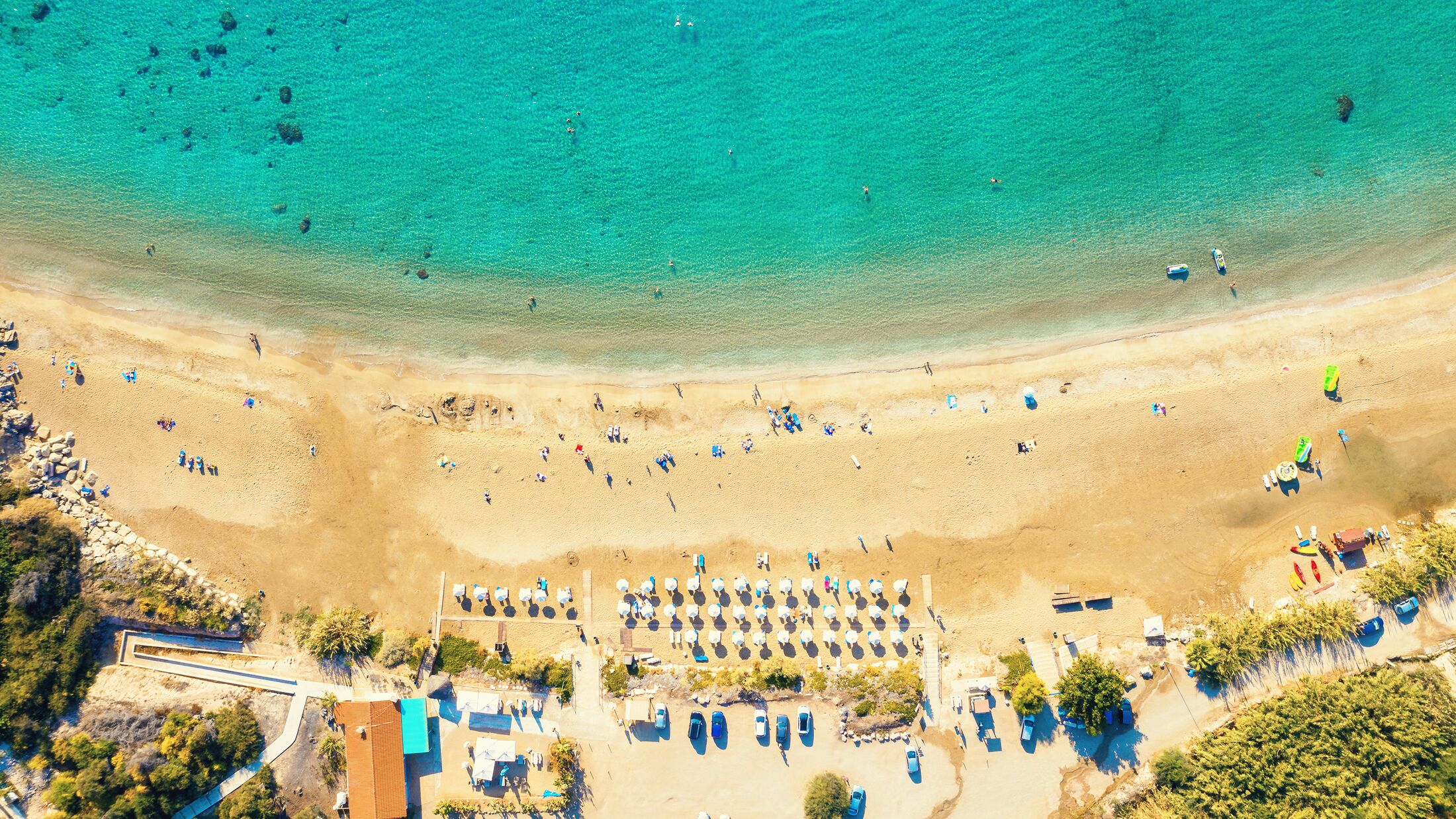 Aerial view of Coral Bay beach - popular beach with clear sea water and comfortable sandy beach, many tourists, sunbeds with umbrellas in Peyia village, Cyprus.